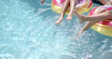 Genç kadınlar renkli havuzun üzerinde otururken ayaklarıyla su sıçratırlar, fotokopi alanı ile. Havuzda güneşli bir gün, neşeli bir anı yakalıyorum, yavaş çekim..