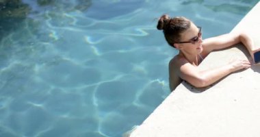 Bun saç stili olan genç beyaz kız havuz kenarında fotokopi çekmeyi seviyor. Güneş gözlüğü ve mayo takıyor, rahat bir günün özünü yakalıyor, ağır çekim..