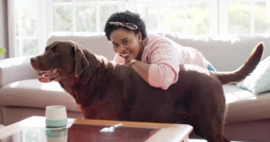 Afrikalı Amerikalı bir kadın evde büyük kahverengi bir Labrador köpeğini kucaklıyor. Güneş ışığı pencerelerden süzülür. Sahibi ve evcil hayvanı arasındaki bir sevgi anını ön plana çıkarır..