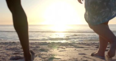 Gün batımında kumlu bir plajda dört farklı insan ayakta duruyor. Dalgalar yavaşça ayaklarına vuruyor. Günlük plaj kıyafetleri, günün sonunda sakin bir tatil atmosferi öneriyor, yavaş çekim..