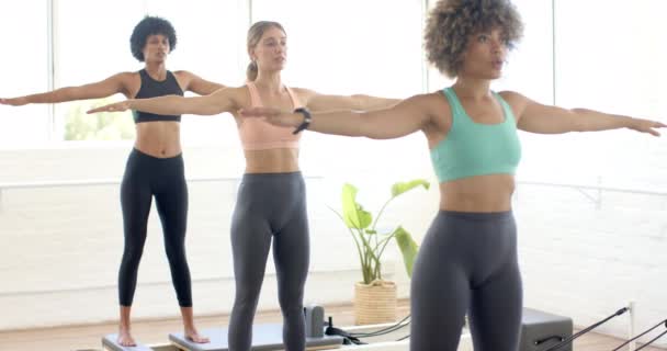 ヨガを練習する3人の女性が腕を伸ばしました 彼らは明るい部屋にあり ポーズのバランスと調和を維持することに焦点を当てています スローモーション — ストック動画
