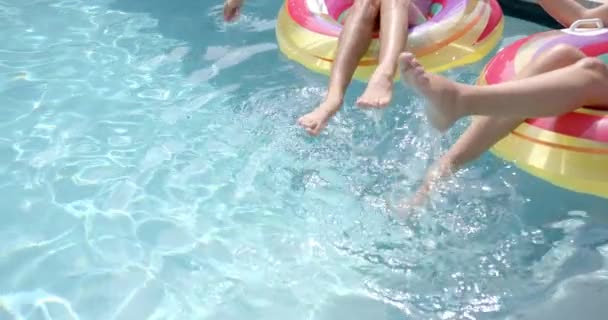 若い女性は コピースペースとカラフルなプールフロートに座っている間 足で水を飛ばします それはプールで晴れた日であり 遊び心のあるレジャー スローモーションの瞬間をキャプチャします — ストック動画
