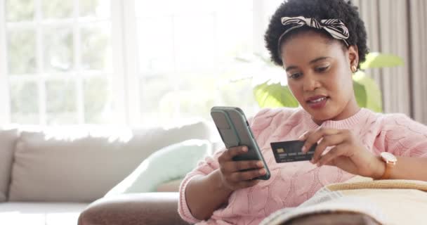 非洲裔美国妇女在家里用智能手机进行网上购物 并留有复制空间 她穿着一件粉色毛衣和一条发带 在灯光明亮 动作缓慢的客厅里把注意力集中在她的装置上 — 图库视频影像