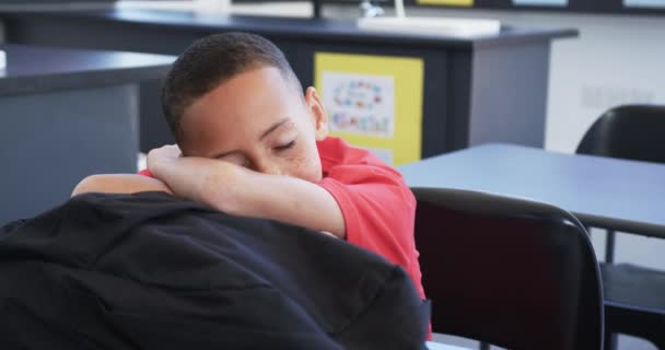 赤いシャツを着てバカな男の子は 学校の教室で彼の腕を休ませている 休憩中 または疲れた 遅い動きを感じている間に 教室の設定にいるようです — ストック動画