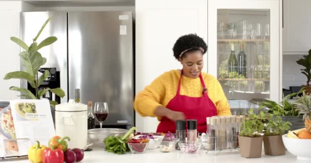 回放一位非洲裔美国妇女在现代厨房准备食物的烹饪表演 她穿着一条红色围裙 用的是威士忌 周围都是新鲜的配料 动作缓慢 — 图库视频影像