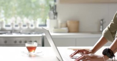 Genç bir Afrikalı Amerikalı kadın dizüstü bilgisayarına odaklanmış, fotokopi alanı olan, evdeki mutfakta. Saçlarını örüyor, günlük giysiler giyiyor ve İç İşleri 'ni yönetiyor. Ağır çekimde, değiştirilmemiş..