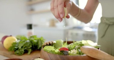 Bir insan salatanın üzerine otlar serpiyor. Taze malzemeler onları parlak bir mutfakta sarar. Bu da sağlıklı bir yemek hazırlığını, ağır çekimde ve değişmeden olduğunu gösterir..