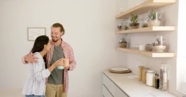 Çeşitli bir çift evdeki modern bir mutfakta bir anı paylaşıyor, kopyalama alanı. İspanyol kadın ve beyaz adam, ikisi de genç, birlikte içecekten zevk alırken gülümsüyorlar, değişmeden, ağır çekimde..