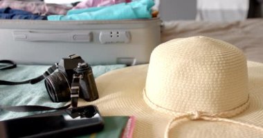 Seyahat gereksinimleriyle dolu bir bavul. Kamera, şapka ve akıllı telefon birinin yolculuk için hazırlandığını gösteriyor. Tatil, ağır çekim, değiştirilmemiş..