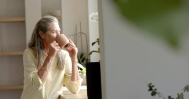 Olgun, beyaz bir kadın evinde sıcak bir içecekten hoşlanır, fotokopi çekmekten. Uzun gri saçları, düşünceli bir ifadesi var. Sıradan sarı bir bluz giyiyor. Ağır çekimde, değişmemiş.