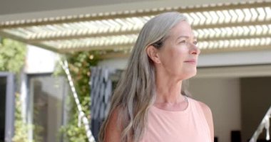 Olgun, beyaz bir kadın evinde fotokopi odasıyla dışarıda sıcak bir şekilde gülümsüyor. Gümüş rengi saçları, açık renk kırışıklıkları var ve kolsuz, ağır çekimde, değişmemiş bir bluz giyiyor..