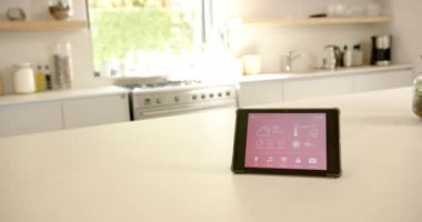 Akıllı bir ev arayüzü mutfak tezgahında durur, kopyalama alanı. Cihaz çeşitli kontrolleri gösteriyor, modern, parlak mutfak atmosferiyle harmanlanmış, değiştirilmemiş, yavaş çekim