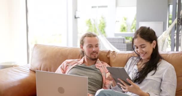 一对多样化的夫妇在家里的沙发上使用平板电脑 白人男子和西班牙女子都很年轻 穿着随意 分享着一段数字互动的时光 没有改变 — 图库视频影像