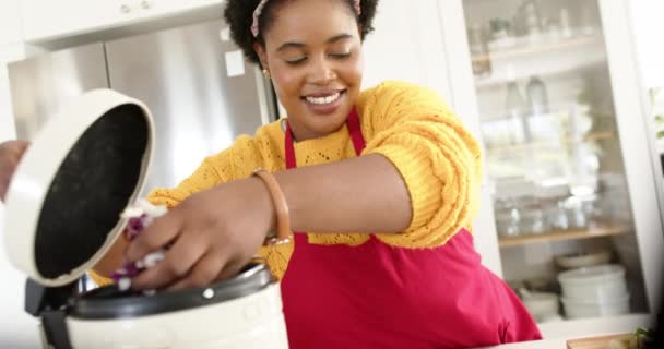 アフリカ系アメリカ人女性がコンポスト ビンに食品廃棄物を投じた 彼女は黄色いセーターの上に赤いエプロンを着て 彼女の笑顔は料理芸術への情熱を示唆しています スローモーション 変更されていない — ストック動画
