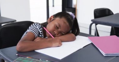 Bir okul sınıfında, melez genç bir kız işine odaklanıyor. Uzun, koyu saçlı, çizgili bir gömlek giyiyor, ve bir deftere yazıyor, değiştirilmemiş, ağır çekimde..