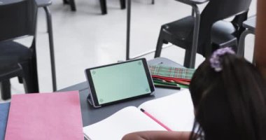 Bir okul sınıfında, genç bir Asyalı kız fotokopi aletiyle elini kaldırır. Uzun siyah saçları, pembe saçlı bir aksesuarı var ve yeşil ekranlı bir tabletin yanındaki bir not defterine yazı yazıyor..