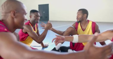 Bir grup arkadaş basketbol sahasında oturuyor. Afro-Amerikalı erkekler kırmızı ve sarı basketbol formaları giyiyorlar, arkadaşça sohbet ediyorlar, değişmeden, ağır çekimde.