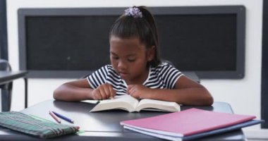 Okulda, bir sınıfta, genç bir Afrikalı Amerikalı kız bir kitap okumaya odaklanıyor. Siyah saçlı, mor bir aksesuarla bağlanmış, çizgili bir bluz giyiyor, değişmemiş, ağır çekimde..