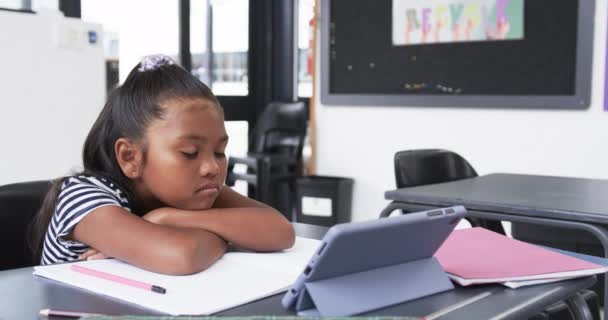 学校の教室では 若いアフリカ系アメリカ人の少女がコピースペースのあるタブレットに焦点を当てています 彼女は背中に結ばれた暗い髪をしており ストライプトップを着用し 意図的にリサイクルポスターの横に研究しています — ストック動画