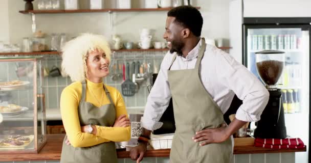 在一家舒适的咖啡店里 一位多样化的巴里斯塔团队的同事一起分享了片刻 这位年轻的非裔美国男人和白人女人都穿着围裙 热情地 一丝不苟地 慢吞吞地交谈着 — 图库视频影像
