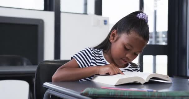 Koulun Luokkahuoneessa Kaksirotuinen Nuori Tyttö Keskittyy Kirjan Lukemiseen Hänellä Mustat — kuvapankkivideo