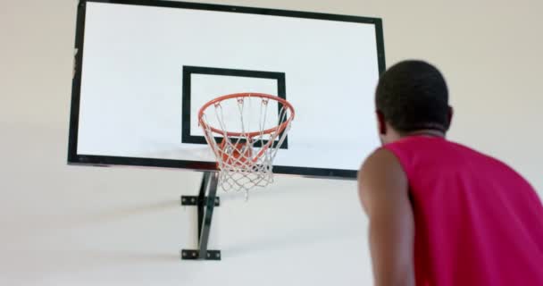 中年のアフリカ系アメリカ人がバスケットボールを撃っている 彼はフープに焦点を当てて黄色と赤のバスケットボールのユニフォームを着ています 変更されていない スローモーション ストック動画