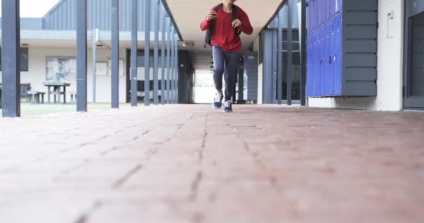学校の廊下では 若い白人少年がコピースペースで動いている 彼は軽い肌 暗い髪を持っており 赤いバックパックと青いスニーカーを着ています 変更されていない スローモーション — ストック動画