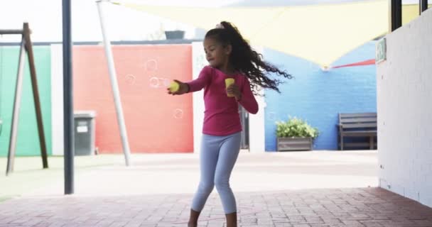 Koulun Leikkikentällä Nuori Afroamerikkalainen Tyttö Puhaltaa Kuplia Hänellä Kiharat Tummat — kuvapankkivideo