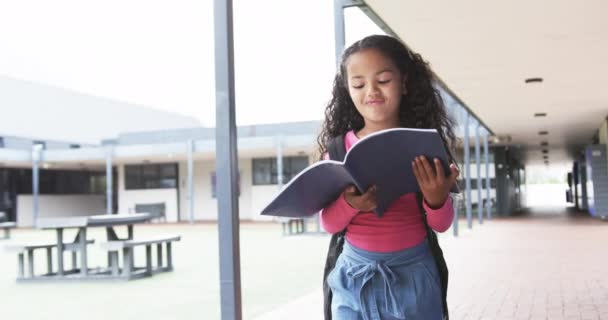 学校の廊下では 若い女性が本を読むことに夢中になっています 彼女はカーリーダークな髪をしていて ピンクのトップを着て デニムのスカートは 焦点を当てた表情で 変わらない — ストック動画