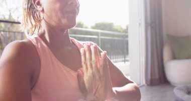 Kıdemli bir Afrikalı Amerikalı kadın, evinde fotokopi alanı olan güneşli bir odada meditasyon yapıyor. Cildi yaşlanma belirtileri gösteriyor, ve saçları pembe bir saç bandı ile şekillendirilmiş, değiştirilmemiş, yavaş çekim.