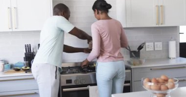 Çeşitli bir çift modern bir mutfakta birlikte kahvaltı hazırlıyor. Afrika kökenli Amerikalı koca ve İspanyol kadın, ikisi de genç, bir yemek hazırlamaya odaklanmışlar, koca tencereyi karıştırmış ve karısı da bakmış, değişmemiş..