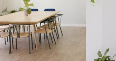 Minimalist bir mutfakta büyük masa ve mavi sandalyeler bulunur. Ahşap çerçeveler beyaz duvarları süslüyor, odanın temiz ve modern estetiğini tamamlıyor, değiştirilmemiş, yavaş çekim