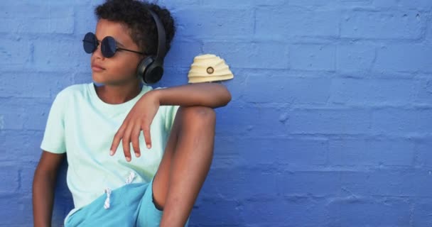 Nuori Afroamerikkalainen Opiskelija Rentoutuu Sinistä Taustaa Vasten Kopiotilalla Urheilu Aurinkolasit kuvapankkivideo