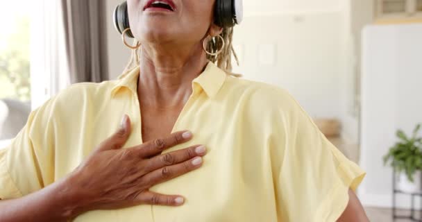 一位非洲裔美国老年妇女居家调解和戴耳机 眼睛闭着 她的表情是一种深沉的感情 唱着或欣赏着最喜爱的曲调 一动不动 动作缓慢 — 图库视频影像