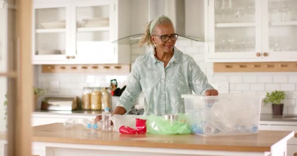 アフリカ系アメリカ人女性がキッチンでリサイクルしています 彼女は短い灰色の髪 眼鏡を持っており 彼女のタスク 変更されていない ゆっくりとした動きに焦点を当てながら軽いブルーのシャツを着ています — ストック動画