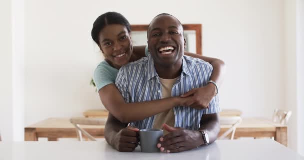 アフリカ系アメリカ人の若いカップルは 自宅で楽しい瞬間を共有しています 夫はカメラで波を起こし 妻は彼を後ろから抱きしめながら どちらも暖かく 変わらず ゆっくりとした動きをしています — ストック動画