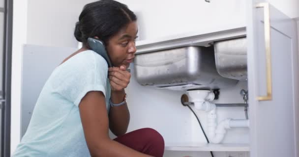 アフリカ系アメリカ人の若い女性がシンクを直している 彼女は 彼女が配管で動作するようにマルチタスク 彼女の肩と耳の間にくっついた電話を持っています 変更されていない スローモーション — ストック動画
