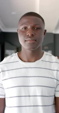 Dikey video: Genç bir Afrikalı Amerikalı adam kameraya gülümsüyor. Kısa siyah saçları, çizgili gömleği ve kendinden emin, arkadaş canlısı bir tavrı var.