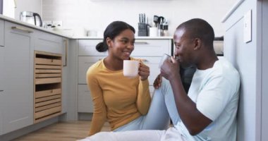 Genç bir Afrikalı Amerikalı çift mutfaklarında kahve içerek eğleniyor. Kocasının kısa siyah saçları var ve karısının saçı arkadan bağlanmış, sarı bir bluz giyiyor..
