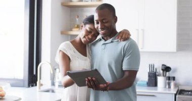 Çeşitli bir çift evdeki mutfakta bir tablet kullanıyor. Afro-Amerikalı koca ve karısı, her ikisi de sıcak bir gülümsemeyle, içeriğine bakıyorlar, değişmeden, ağır çekimde.