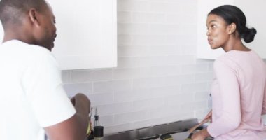 Çeşitli bir çift modern bir mutfakta birlikte kahvaltı hazırlıyor. Afrika kökenli Amerikalı koca ve karısı, her ikisi de genç, bir yemek hazırlamaya odaklanmış durumdalar..