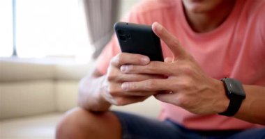 Genç bir çift ırklı adam akıllı telefonuna odaklanmış. Akıllı bir kaset ve günlük pembe tişört giyiyor. Kapalı bir yerde oturuyor. Değiştirilmemiş, ağır çekimde..