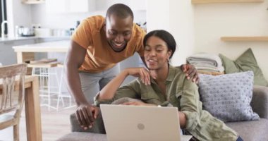 Çeşitli bir çift evdeki kanepede dizüstü bilgisayarlarıyla eğleniyor. Afrika kökenli Amerikalı koca, karısı otururken, ekranlara bakıyor, değişmeden, ağır çekimde..