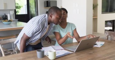 Çeşitli bir çift evde dizüstü bilgisayar kullanarak finansman yönetiyor. Afrika kökenli Amerikalı koca ve karısı, ikisi de koyu saçlı, dizüstü bilgisayara ve faturalara odaklanmış, değiştirilmemiş, yavaş çekim