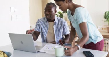 Çeşitli bir çift evde dizüstü bilgisayar kullanarak faturalarını ödeyerek ciddi bir tartışmaya giriştiler. Siyah kıvırcık saçlı Afrikalı koca ve karısı bir dizüstü bilgisayarın yakınındaki faturaları ve faturaları inceliyor..