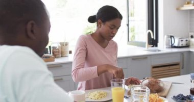 Afro-Amerikalı çift güneşli bir mutfakta kahvaltıyı sever. Koca, karısı gibi, saçı topuz şeklinde, ekmeği dilimliyor, değiştirilmemiş, ağır çekim.