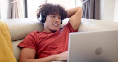 Melez bir genç evdeki kanepede dizüstü bilgisayarıyla rahatlıyor. Kıvırcık saçları, parlak bir gülüşü var. Sıradan kırmızı bir gömlek giyiyor. Değiştirilmemiş, ağır çekim.