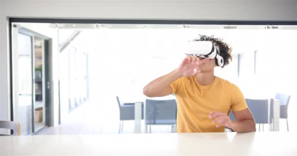 一个年轻的白人男子正在厨房里使用一个带有复制空间的虚拟现实耳机 他卷曲的头发 穿着一件黄色的衬衫 指着上方 沉浸在虚拟现实之中 一动不动 动作缓慢 — 图库视频影像