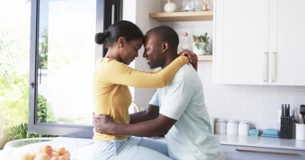 一对多样化的夫妇在厨房里分享着一个温柔的时刻 亲切地拥抱在一起 这位非洲裔美国人的丈夫和他的妻子都很年轻 他们亲切地拥抱在一起 妻子穿着一件黄色的上衣 把头发绑在后面 — 图库视频影像