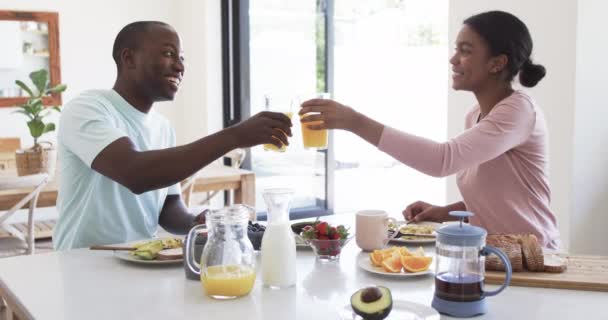 アフリカ系アメリカ人の若いカップルは キッチンで一緒に朝食を楽しんでいます 夫は短い黒い髪をしていて 妻は彼女のカーリーな髪を縛って オレンジジュースのグラスを保持しています 変更されていません ロイヤリティフリーのストック動画